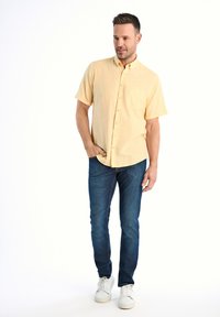 Lichtgele kortekraag overhemd met knopen, blauwe slim-fit jeans en witte sneakers. Het overhemd heeft een borstzak en een casual ontwerp.