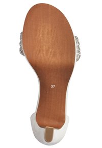 Hvide hælede sandaler med en brun, tekstureret sål. Har et dekorativt design nær hælen og med størrelsen angivet som 37.