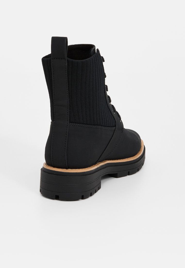 Czarne botki za kostkę z ribbową cholewką, sznurowanym przodem i teksturowaną gumową podeszwą. Z tyłu znajduje się uchwyt do łatwego zakładania.