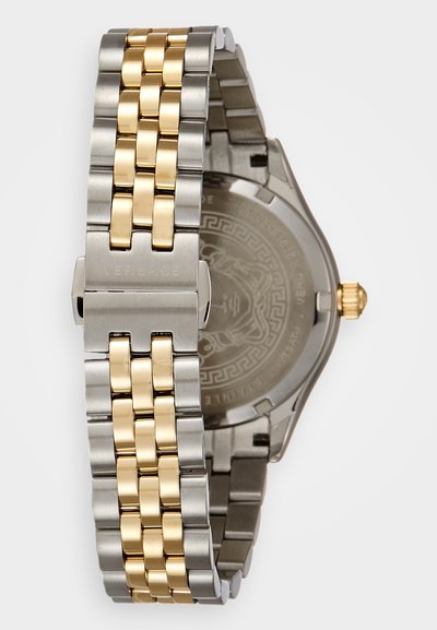 Tvåfärgad metallklocka med ett armband i rostfritt stål i silver- och guldtone. Har ett runt hölje och en graverad baksida med logodetaljer.