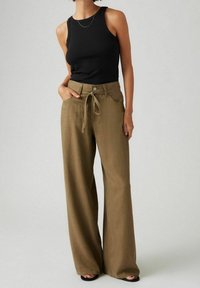 Top negro de canalé combinado con pantalones de pierna ancha en color verde oliva, con cintura anudada y bolsillos delanteros. Tejido suave y ajuste relajado.