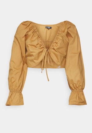 Blusa amarela mostarda cortada com mangas longas em puf, frente franzida e fecho com cordão. Tecido de algodão suave com punhos elásticos.