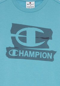 T-shirt de algodão azul claro com um estampado de malha preta do logotipo "Champion" com uma aparência texturizada e um decote redondo.