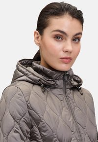 Padded jacket w stonowanym szarym kolorze, z haftowanym wzorem, kapturem ze sznurkiem i zapięciem na zamek z przodu.