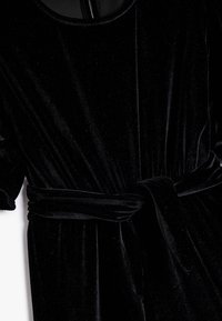 Zwart fluwelen jumpsuit met korte pofmouwen, een ronde hals en een stoffen riem in de taille voor een getailleerd silhouet.