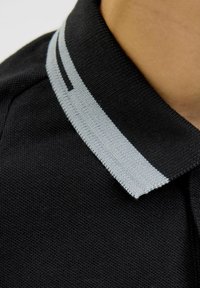 Juodas polo marškinėliai, pagaminti iš tekstūruoto audinio, su pilkai dryžuotu apykakle ir subtiliu pilku akcentu apykaklės krašte.