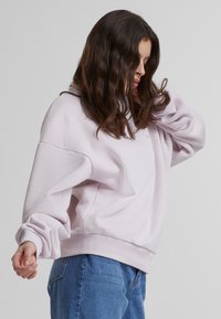 Lyselilla sweatshirt med oversized passform, ribbede mansjetter og kant. Myk tekstur, minimalistisk design med subtile merkevaredetaljer.