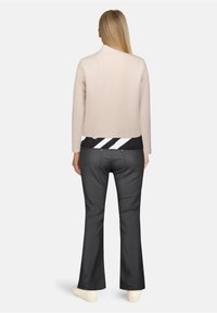 Jasnoróżowa kurtka o fakturze z kołnierzem, w komplecie z czarną i białą paskowaną bluzką oraz czarnymi spodniami dzwonowymi z dyskretnymi detalami z tyłu.