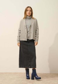 Cárdigan gris sobre un suéter de cuello alto gris claro, combinado con una falda maxi de mezclilla oscura y botas de tobillo azul brillantes con tacón cuadrado.