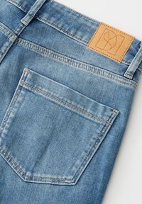 Lichtblauwe spijkerbroek met een gestructureerd oppervlak, voorzien van een beige leren patch aan de tailleband en een enkele achterzak met stikseldetails.