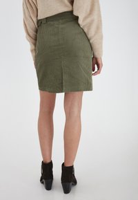 Olivgrön kordkjol med en figursydd midja och vertikal ribbing, kombinerad med svarta ankelstövlar med klossklack.