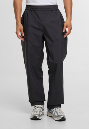 Zwarte, lichte, waterdichte broek met een elastische tailleband, voorzien van zijzakken en een relaxte pasvorm voor comfortabele beweging.
