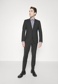 Abito nero con una vestibilità su misura, camicia bianca con motivo a quadri blu navy e mocassini neri. Tessuto liscio, spalle strutturate e pantaloni slim.