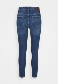 Jeans ajustados de denim azul oscuro. Presentan una cintura alta, dos bolsillos traseros con un detalle de costura en zigzag y una etiqueta de cuero en la parte posterior.