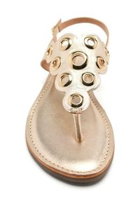 Sandalia de cuero bronce con diseño de tira entre los dedos, presenta acentos circulares dorados y suela plana. Correa ajustable en el tobillo para un ajuste seguro.