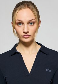 Camisa polo de color azul marino con escote en V, cuello corto y un sutil logo de "POLO CLUB". Textura suave y diseño ajustado. Sin patrones ni acentos visibles.