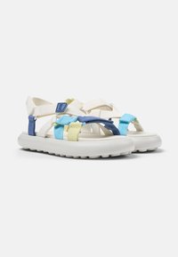 White sandals with a rubber sole featuring multicolored woven straps in blue, green, and yellow. Adjustable buckles enhance fit.
