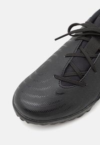 Chaussure de sport noire texturée avec une surface lisse, un design à motifs et un système de laçage. Dispose d'une semelle robuste pour une meilleure traction.