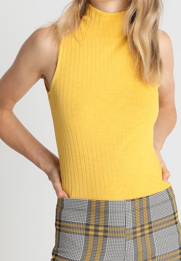 Žlutý bezrukávový žebrovaný top s vysokým límcem, spojený s kalhotami s kostkovaným vzorem v černé a žluté barvě. Materiál vypadá měkký a strukturovaný.