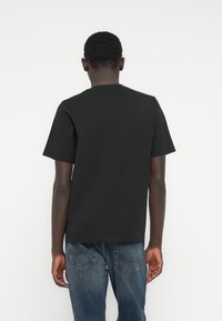 Μαύρο βαμβακερό κοντομάνικο μπλουζάκι με λαιμόκοψη σε στρογγυλή γραμμή, με απλό σχέδιο και άνετη εφαρμογή, προβολή από πίσω.