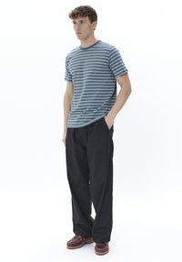 Striped blue and gray t-shirt, relaxed fit, paired with black wide-leg pants and maroon shoes with a textured sole. Plain white background.