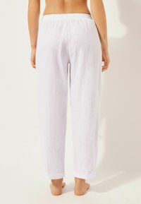 Pantalons en lin blanc avec une taille élastique, des ourlets roulés et une coupe décontractée, présentant une texture lisse et respirante.