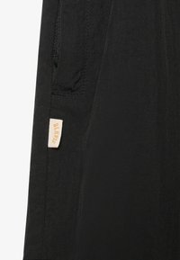 Tessuto nero con una texture liscia e una leggera lucentezza; presenta una tasca e un'etichetta beige stampata con la scritta "BLK" in un carattere serif.