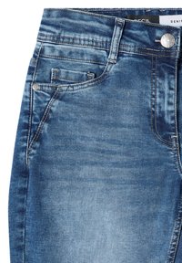 Gros plan sur un jean en denim bleu montrant la poche avant, la petite poche à monnaie, les détails de couture, la passants de ceinture et la fermeture par bouton en métal.