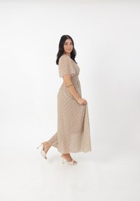 Maxikjole i lyse beige stof med blomsterprint, kortærmede, smocket talje og flydende nederdel. Kombination med strapsandaler.