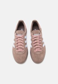 Καφέ sneakers από σουέτ με ροζ κορδόνια και τρεις λευκές ρίγες. Στρογγυλερή μύτη, μαλακός εσωτερικός πάτος και λαστιχένια εξωτερική σόλα. Κλασικός σχεδιασμός.