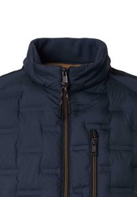 Marineblau gepolsterte Jacke mit engem Kragen, zwei mit Reißverschluss verschlossenen Taschen und kontrastierenden braunen Reißverschlüssen. Verfügt über strukturierten Stoff auf den Schultern.