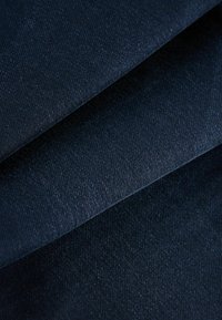 Tejido de mezclilla azul oscuro con un patrón de tejido de sarga visible. La textura parece suave con un ligero brillo, doblada en capas.
