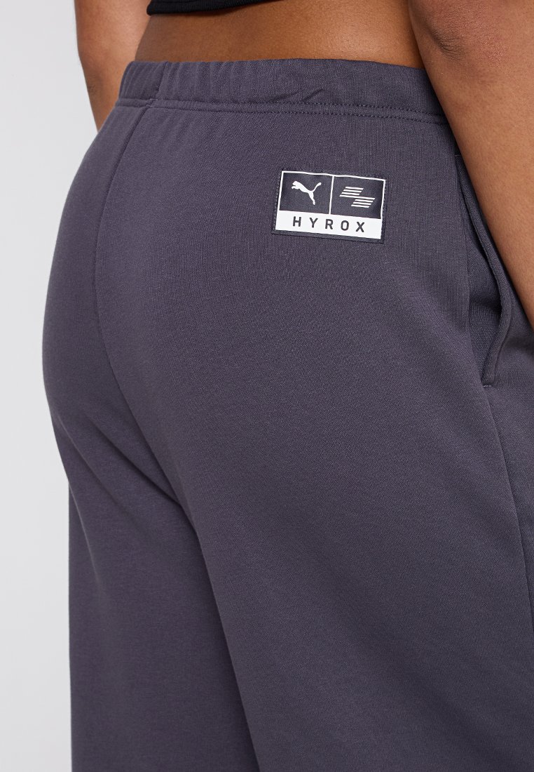 Graue Hose aus weichem Baumwollmix, mit einem elastischen Bund und einem kleinen Markenlabel auf der Rückseite, das "HYROX" zeigt.