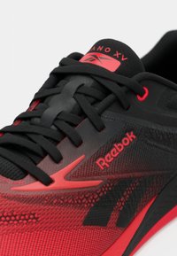 Must must ja punane Reebok spordijalats, mustade paelte ja punaste silmadega, näidates tekstuuriga ülemist osa ja brändi detaile.