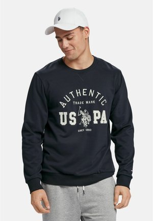 Marineblå genser med rund hals, ribbestrikkede ermer og kant. Har en hvit trykket logo "AUTHENTIC US PA" og et motiv av polo spillere.