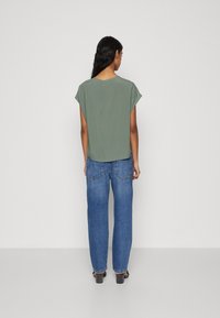 Grønn kortermet topp med løs passform, kombinert med blå høytlivede vidde-jeans. Outfiten har en jevn tekstur og enkelt design.