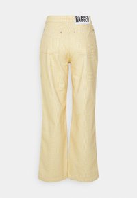 Calças amarelas com um padrão geométrico quadrado, feitas de um material leve. Apresentam uma etiqueta RAGGED Jeans na cintura.