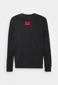 Felpa nera con scollo rotondo, maniche lunghe e polsini a costine. Presenta un'etichetta rettangolare rossa con "HUGO" in testo bianco.