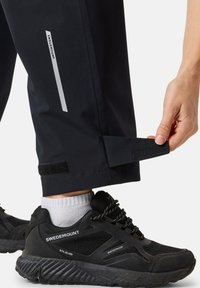 Waterproof black pants with reflective accents and Velcro adjusters at cuffs, paired with black waterproof shoes and white socks.