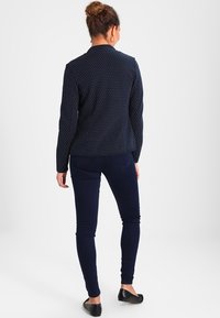 Blazer navy a pois con maniche lunghe, design aderente, tessuto strutturato. Abbinato a jeans skinny blu scuro e scarpe flat nere.