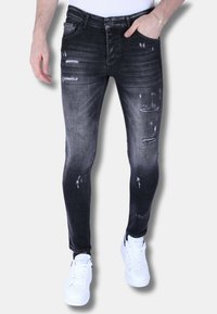 Zwarte skinny jeans met een vervaagd ontwerp en meerdere slijtageplekken, gemaakt van denim stof. Gecombineerd met witte sneakers.