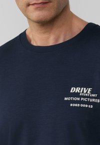 Navyblauw T-shirt van zacht materiaal, met een ronde hals en witte bedrukte tekst: "DRIVE STUNT UNIT MOTION PICTURES 9362:309:13".