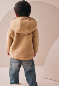 Veste à capuche en polaire beige avec une texture douce, associée à un jean en denim bleu ample doté de poches cargo. Design simple et fonctionnel.