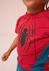 Rød Spider-Man t-shirt med grafik, der viser en stor sort edderkop på forsiden, med blå accenter på siderne. Korte ærmer.
