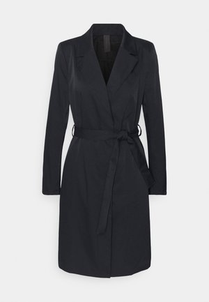 Sort knælange trenchcoat med lange ærmer, reverskrave og bælte i taljen på en lysegrå baggrund.