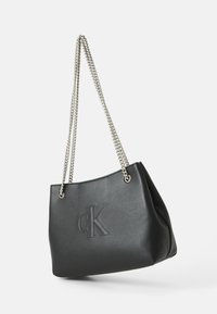 Musta nahkainen olkalaukku, jossa on hopeinen ketjuhihna, etuosassa selvästi kohokuvioitu "CK"-logo ja sileä, jämäkkä muotoilu.