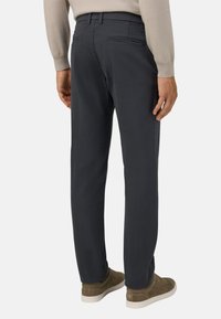 Jūras zila chinos ar taisnu piegriezumu, priekšējām un aizmugurējām kabatām un gludu tekstūru, apvienoti ar gaiši brūnām zamšādas sporta apaviem.