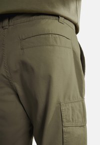 Pantaloni cargo in cotone verde oliva, con dettaglio della tasca posteriore e una texture liscia, dal taglio relaxed. Adatti per un abbigliamento casual.