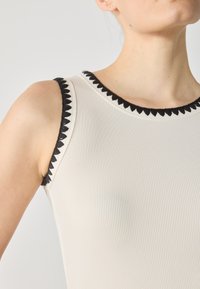 Ribbad linne i off-white med svart v�ågig kant längs halsringningen och ärmhålen. Har en figurnära silhuett och elastisk tyg.