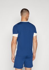 Marinblå atletisk t-shirt med korta ärmar i vitt. Tillverkad av ett ventilerande material, med rund hals och en figursydd design.